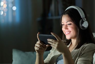 Woman with headphones smiling while holding smartphone