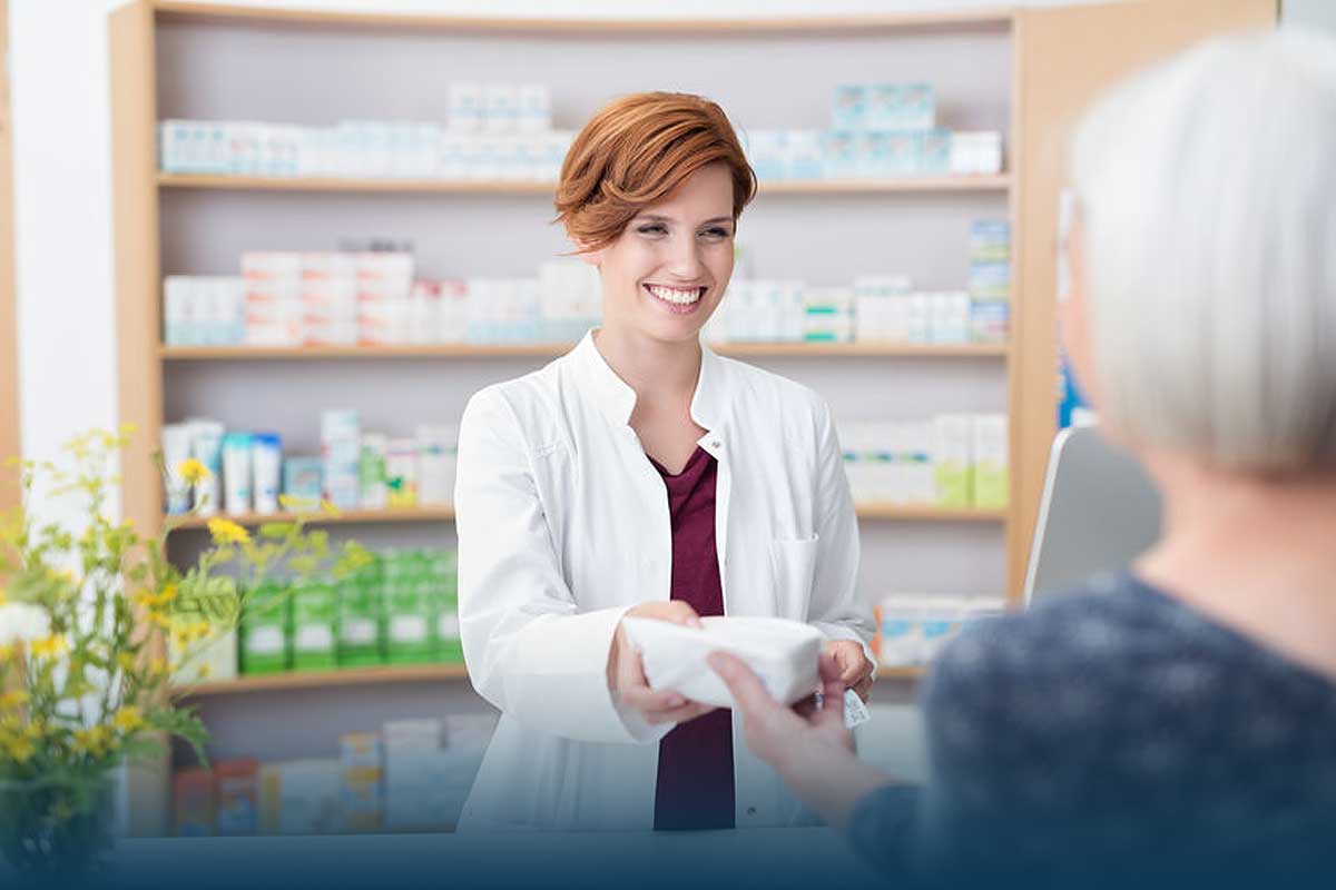 Smiling pharmacist handing prescription to patient over the counter