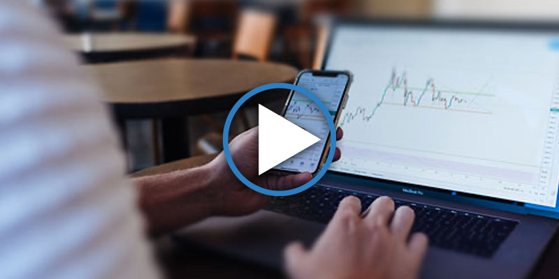 Man looking on phone while stock chart is seen on laptop
